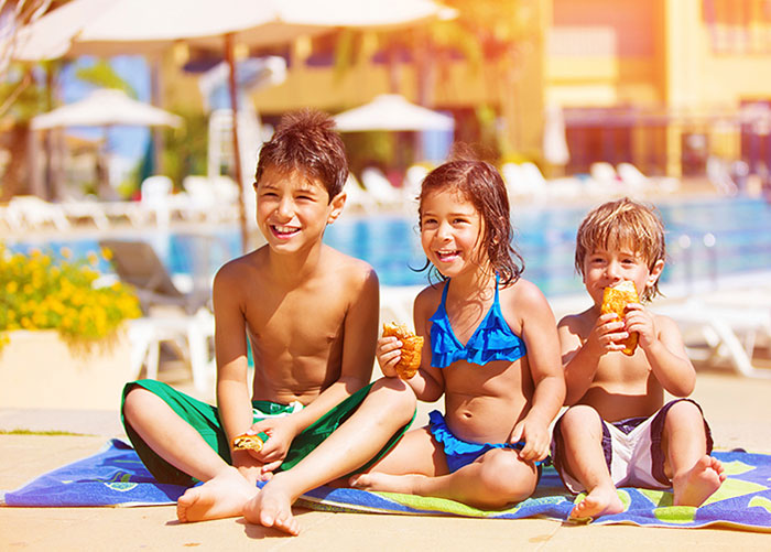 kids sitting on a towel smiling next to pool eating